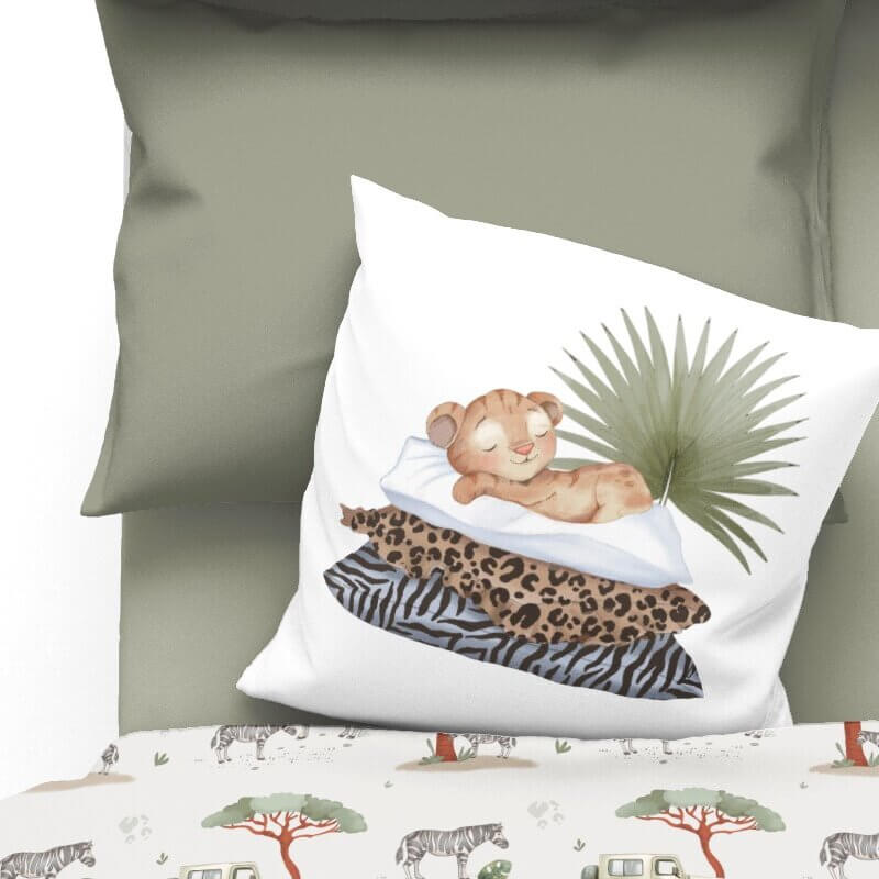 Housse de coussin décorative en coton de 16x16 pouces avec illustration d’un lionceau endormi sur des coussins à motifs animaux et feuille tropicale, posée sur une literie safari.